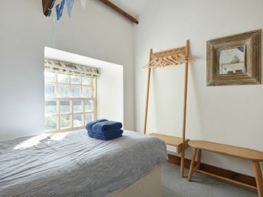 A bedroom with a bed and towels on top with a window and wooden coat rack and mirror at Budle Granary in Bamburgh