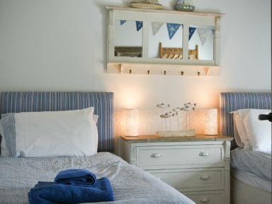 A bedroom with two single beds a white chest of drawers lamps and fish decorations at Budle Granary in Bamburgh