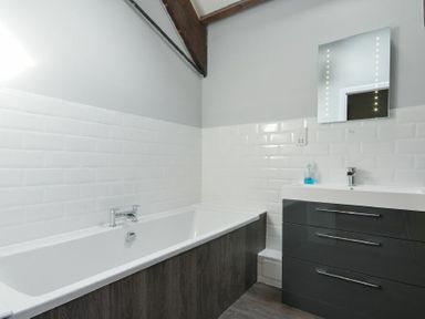 A bathroom with a bathtub, a vanity with drawers, a mirror, and tiled walls at Budle Granary in Bamburgh