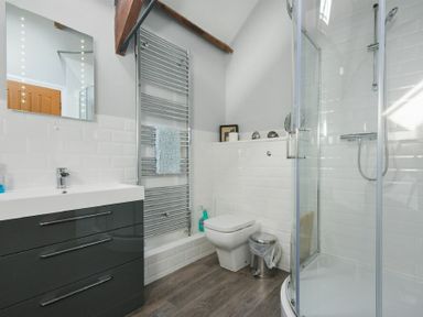 A bathroom with a sink cabinet mirror towel rail toilet trash can and glass shower at Budle Granary in Bamburgh