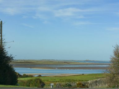 A coastal landscape with water channels and grassy fields under a blue sky at Budle Granary in Bamburgh