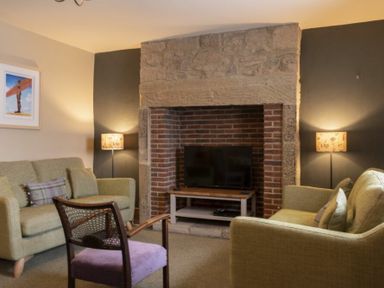A living room with two sofas a chair and a television set in a brick fireplace at Cheshill Cottage in Alnmouth