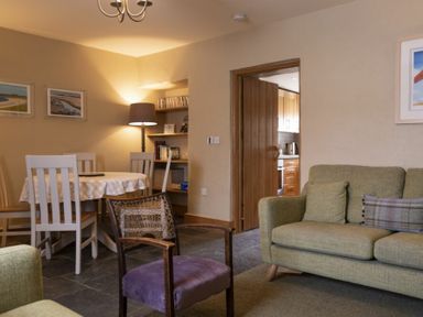 A living room with a green sofa a purple chair a dining table with white chairs and a floor lamp at Cheshill Cottage in Alnmouth