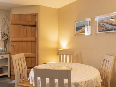A dining area with a round table covered with a tablecloth and four chairs near a wooden door at Cheshill Cottage in Alnmouth