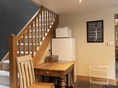 A wooden staircase next to a wooden table with a chair and a refrigerator with a microwave on top at Cheshill Cottage in Alnmouth