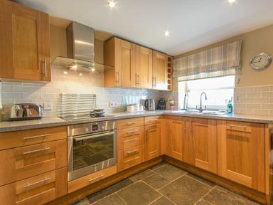 A kitchen with wooden cabinets a stainless steel oven toaster kettle and coffee machine at Cheshill Cottage in Alnmouth