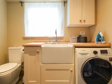 A laundry room with a washing machine a sink an iron and a toilet at Cheshill Cottage in Alnmouth