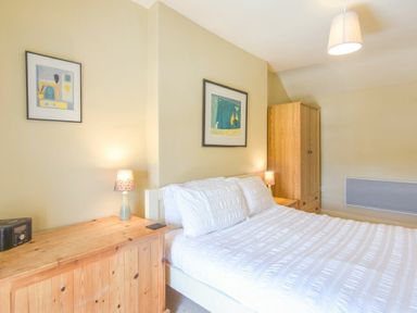 A bedroom with a white bed a wooden wardrobe two lamps and framed pictures on the wall at Cheshill Cottage in Alnmouth