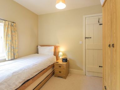 A single bedroom with a bed bedside table lamp wardrobe and a wooden door at Cheshill Cottage in Alnmouth