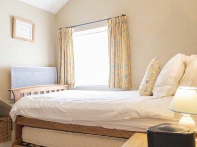 A bedroom with a wooden bed white bedding pillows lamp on nightstand and window with yellow curtains at Cheshill Cottage in Alnmouth