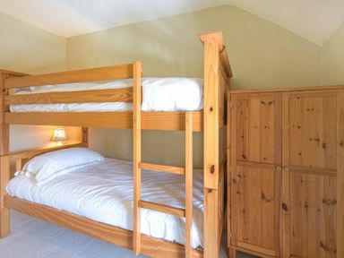 A bedroom with wooden bunk beds and a wooden wardrobe at Cheshill Cottage in Alnmouth