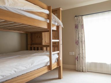 A bedroom with a wooden bunk bed and a window with floral curtains at Cheshill Cottage in Alnmouth