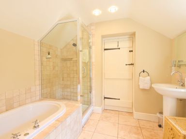A bathroom with a bathtub a glass shower enclosure a sink and a towel hanging near the door at Cheshill Cottage in Alnmouth