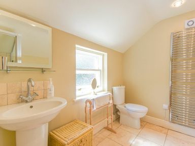A bathroom with a sink mirror toilet towel rack and wicker basket at Cheshill Cottage in Alnmouth