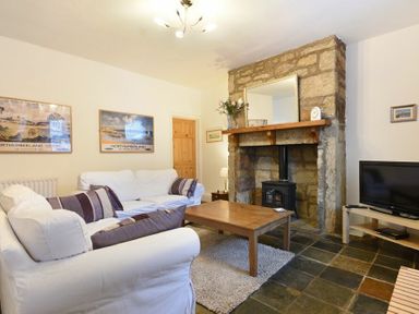 A living room with white sofas wooden coffee table stone fireplace and television at Crier Cottage Alnwick