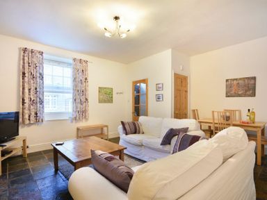 A living room with white sofas purple cushions wooden coffee table dining table and chairs at Crier Cottage in Alnwick