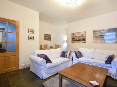 A living room with white sofas wooden coffee table and dining area at Crier Cottage in Alnwick