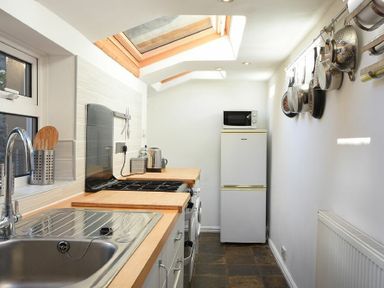 A kitchen with a sink, stove, refrigerator, microwave, and pots hanging on the wall at Crier Cottage in Alnwick