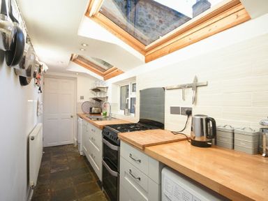 A narrow kitchen with hanging pans stove kettle and skylight windows at Crier Cottage in Alnwick