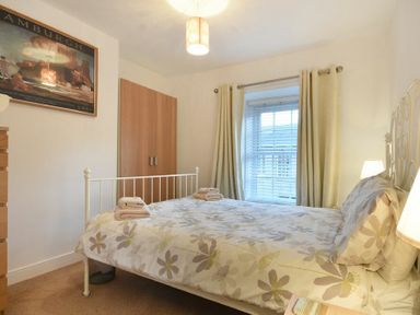 A bedroom with a bed, wooden wardrobe, chest of drawers, window with blinds and curtains at Crier Cottage in Alnwick