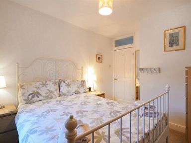 A bedroom with a floral bedspread a white metal bed frame bedside tables lamps and framed pictures at Crier Cottage in Alnwick