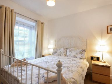 A bedroom with a double bed floral bedding nightstands lamps and closed curtains at Crier Cottage in Alnwick