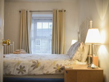 A bedroom with a bed a bedside table with lamps and a window with curtains at Crier Cottage in Alnwick
