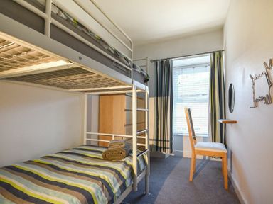 A bedroom with bunk beds a wooden chair a small wall shelf and a window with curtains at Crier Cottage in Alnwick