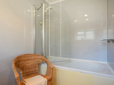A bathroom with a bathtub shower combination and a wicker chair with towels at Crier Cottage in Alnwick