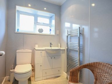 A bathroom with a toilet sink cabinet heated towel rail and a wicker chair at Crier Cottage in Alnwick