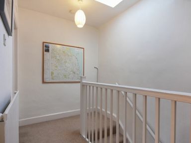 A stairway landing with white railing a framed map on the wall and a ceiling light at Crier Cottage in Alnwick