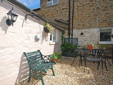 An outdoor patio with a metal bench a table with chairs and potted plants at Crier Cottage in Alnwick