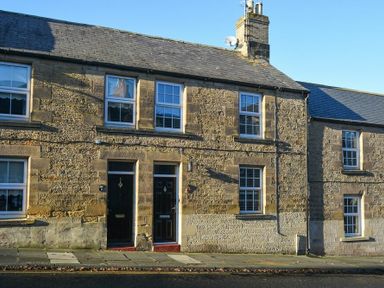 Stone terraced houses with black doors and windows on a street at Crier Cottage in Alnwick
