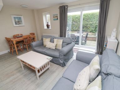 A living room with two blue sofas a white coffee table wooden dining table and chairs sliding glass doors to a patio at Curlew Cottage in Seahouses