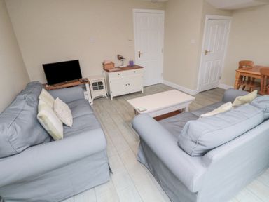 A living room with two blue sofas facing a coffee table and a television on a stand at Curlew Cottage in Seahouses