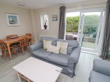 A living room with a blue sofa, wooden dining table with chairs, white coffee table, and sliding glass door at Curlew Cottage in Seahouses