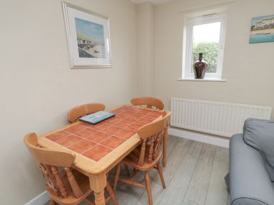 A dining area with a wooden table and four chairs a window with a vase on the sill and two paintings at Curlew Cottage in Seahouses