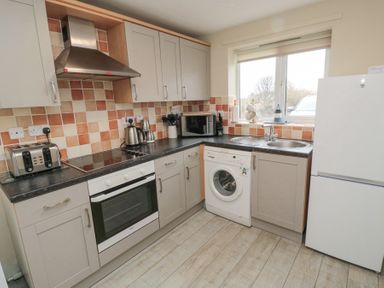 A kitchen with cabinets oven washing machine fridge and window at Curlew Cottage in Seahouses