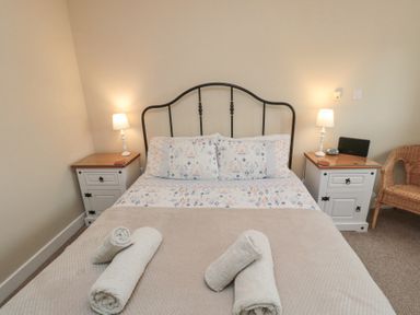 A bedroom with a bed with floral bedding and rolled towels on it two bedside tables with lamps and a wicker chair at Curlew Cottage in Seahouses