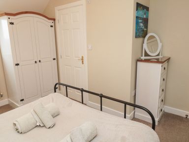 A bedroom with a black metal bed frame towels on the bed a white wardrobe a white chest of drawers with a mirror and a painting on the wall at Curlew Cottage in Seahouses