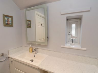 A bathroom sink with a soap dispenser a mirror a small window with a bird decoration and a wall picture of a lighthouse at Curlew Cottage in Seahouses