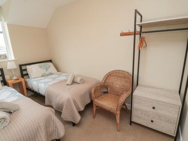 A bedroom with two single beds a wicker chair a small wooden bedside table and a clothing rack at Curlew Cottage in Seahouses