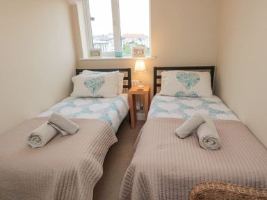 A bedroom with two single beds side by side a wooden nightstand with a lamp between them and a window above Curlew Cottage in Seahouses