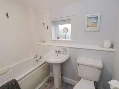 A bathroom with a bathtub sink toilet a small window and a framed picture at Curlew Cottage in Seahouses