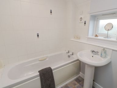 A bathroom with a bathtub a sink a small window and tiled walls at Curlew Cottage in Seahouses