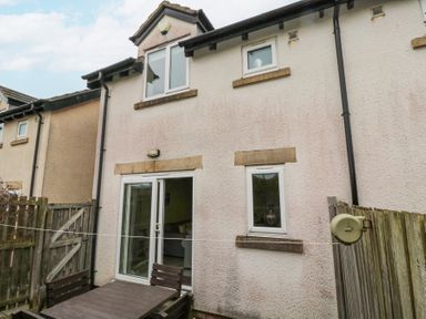 A small outdoor patio area with a wooden table and chairs next to a white two-story house at Curlew Cottage in Seahouses