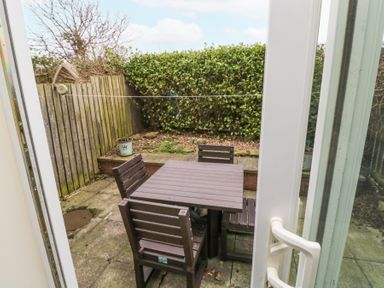 A small outdoor patio with a wooden table and four chairs surrounded by a wooden fence and hedge at Curlew Cottage in Seahouses