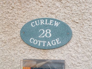 An oval house nameplate with Curlew Cottage 28 on a rough textured wall at Curlew Cottage in Seahouses