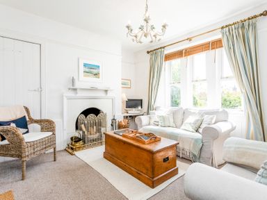A living room with a white fireplace rattan chair wooden chest and light curtains at Elliot Cottage in Bamburgh