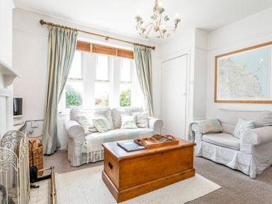 A living room with two sofas a wooden chest coffee table a chandelier and a framed map on the wall at Elliot Cottage in Bamburgh